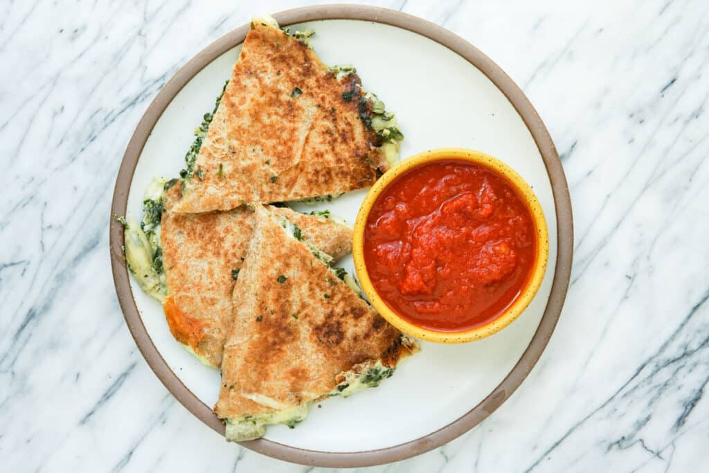 Sliced Spinach Artichoke Quesadillas with Marinara on a plate